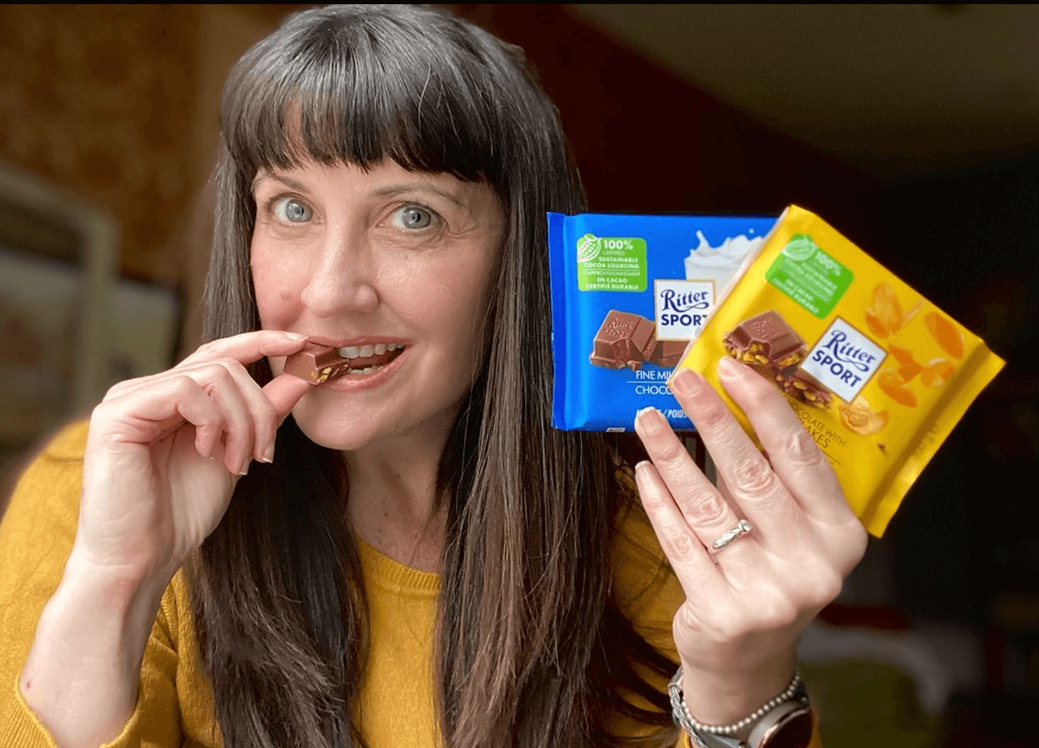 Woman with bangs eating and holding chocolate bars