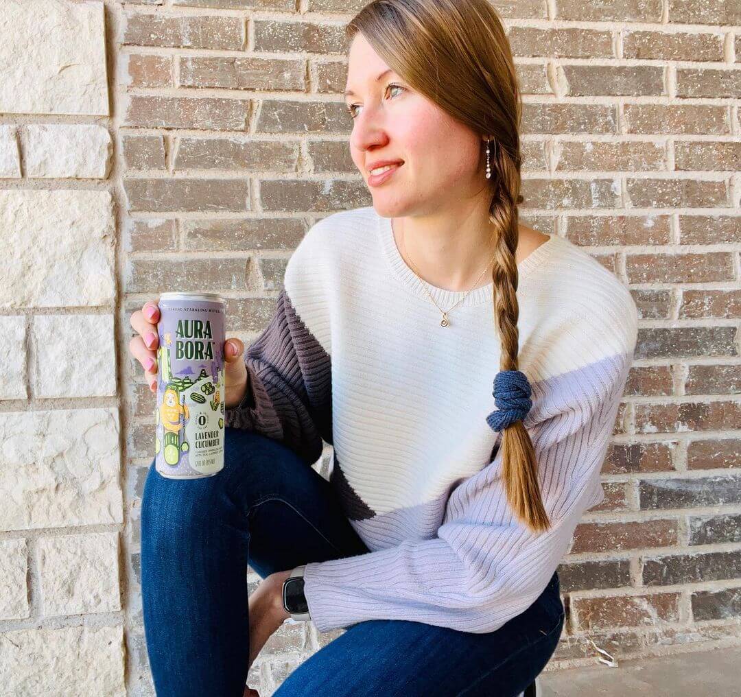 Woman with long pony tail holding a beverage and looking away
